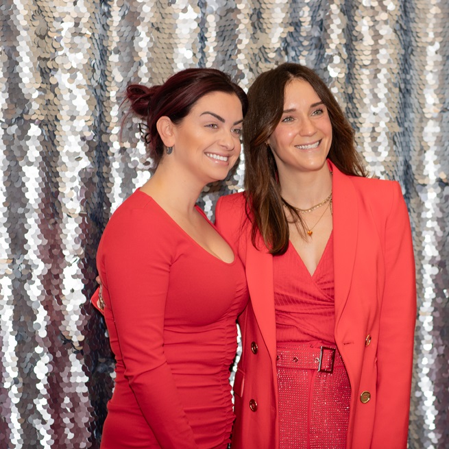 Two women in red standing in front of silver sequin curtain